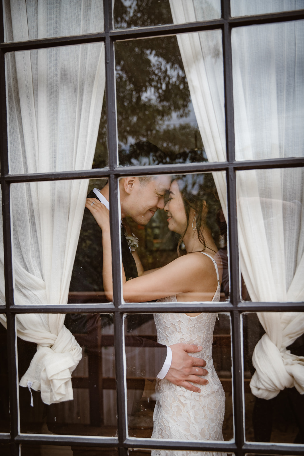 Bride and groom stand in a window and embrace