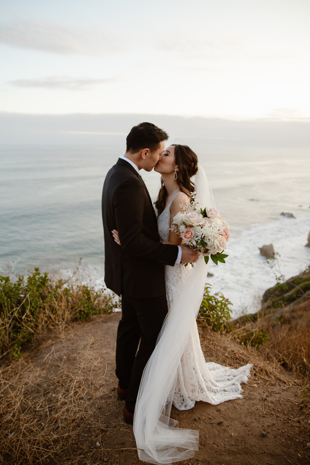 Bride and groom kiss by the ocean