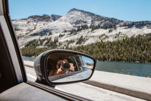 Photographer takes a photo from her car with mountains and lake in the background.