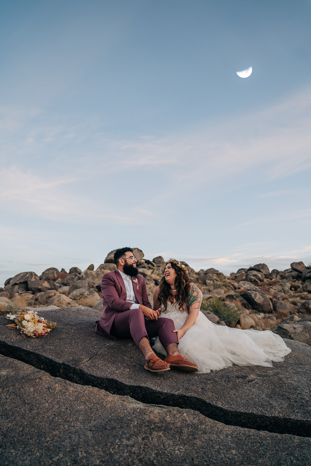 bride and groom sit on rock in the desert