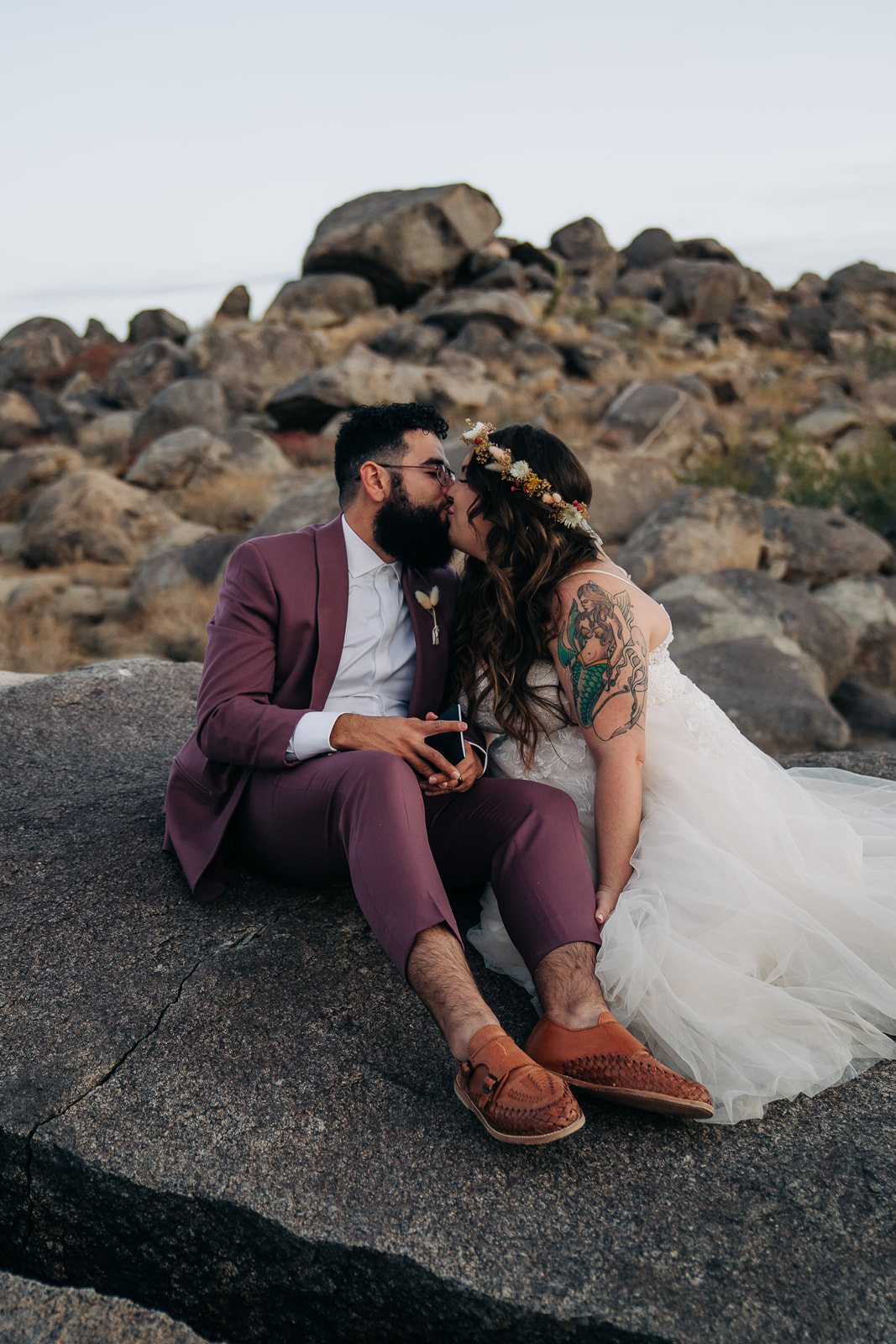 Groom kisses bride while sitting on rock